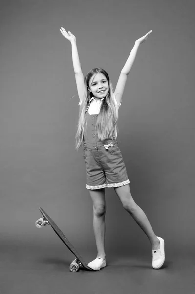 幼年期およびアクティブなゲーム。小さな女の子は、紫色の背景にスケート ボードと笑顔します。気ままな一日。ロングボードを浮かべて子供スケーター。ピンクのジャンプ スーツ子供のスケート ボード。スポーツ活動とエネルギー — ストック写真