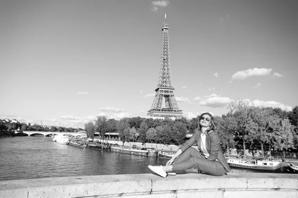 Uma mulher feliz senta-se no rio na Torre Eiffel em Paris, França. Mulher sorrir em óculos de sol no céu azul. Viajando em férias de verão. A sonhar com Paris. Menina com aparência de moda e beleza sensual — Fotografia de Stock