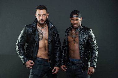 Seksi kıl ve geometrik dövme göğsüne İspanyol adamla. Beyzbol kap gülümseyen Afrika adam. Modelleri kas torsolar giyen deri ceket ve moda aksesuarları, moda kavramı ile