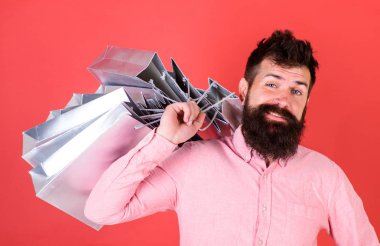 Sakal ve bıyık taşır alışveriş torbaları omuz, kırmızı zemin üzerine olan adam. Satış sezon indirimlerle alışveriş adam. Alışveriş kavramı. Mutlu yüz hipster bağımlısı alışveriş veya Alışverişkoliğin