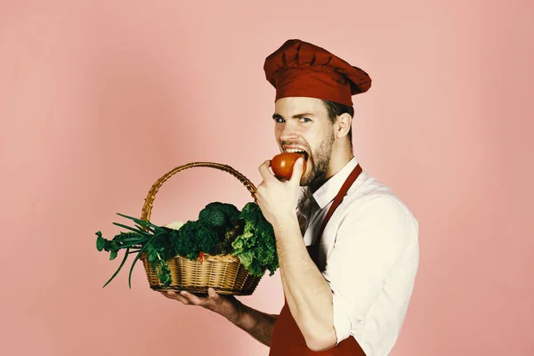 Lo chef in uniforme bordeaux mangia pomodoro. Concetto di cibo sano . — Foto Stock