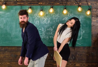 Student lady slapping on teachers buttocks with book. Girl on smiling face having fun while punishes teacher. Role games concept. Man with beard punished by sexy student, chalkboard on background clipart