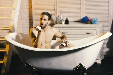 Sakallı adam banyo yapıyor ve köpük üflüyor.