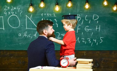 Boy, child in graduate cap play with dad, having fun and relaxing during school break. Teacher with beard, father teaches little son in classroom, chalkboard on background. School break concept clipart