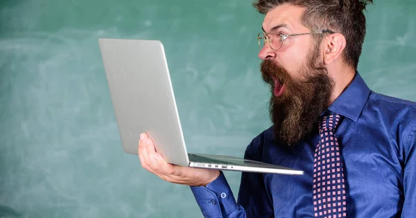 Shocking information. Hipster teacher wear eyeglasses and necktie holds laptop surfing internet. Shocking news. Teacher bearded shocked man with modern laptop surfing internet chalkboard background — Stock Photo, Image