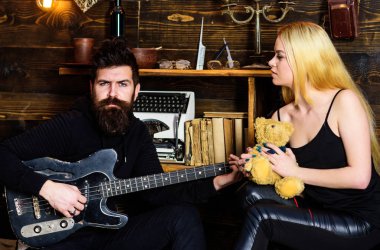 Sakin yüzlü aşık çift romantik atmosferin tadını çıkarıyor. Kadın oyuncak ayıyı elinde tutarken adam gitar çalıyor. Romantik randevu konsepti. Çift romantik bir akşam geçirir, ahşap iç plan.