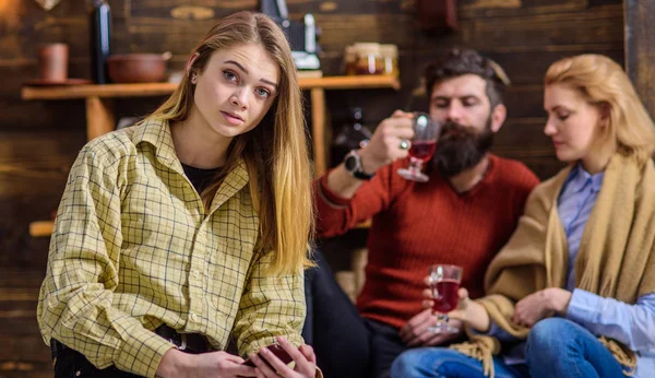 Chica rubia con grandes ojos en camisa amarilla vintage sentado en la sala de estar de campo casa de madera. Barbudo hombre y su esposa charlando, bebiendo y divirtiéndose mientras su hija se sienta sola —  Fotos de Stock