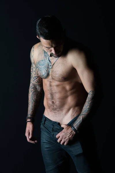 Uomo spogliarellista mostra busto sexy. Sportsman con sei pack e addominali stripping. Atleta con muscoli bicipiti e tricipiti. Uomo di moda con tatuaggio decollare jeans. Desiderio di sessualità e attrazione — Foto Stock