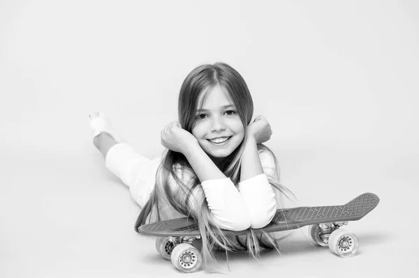 Sonrisa de niña pequeña con tabla de skate sobre fondo rosa. Patinador infantil sonriendo con longboard. El chico de la patineta yace en el suelo. Estilo de vida infantil y juegos activos. Actividad deportiva y energía, pastel picante — Foto de Stock