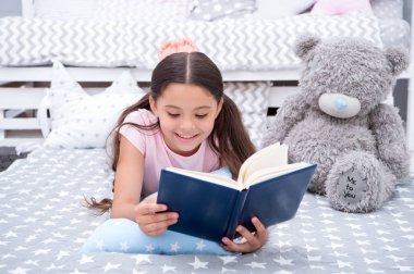 Masal yatakta okuyun. Kız çocuk yatak kitap okumak bir oyuncak ayı ile yatıyordu. Çocuk yatmaya hazırlanın. Akşam masal zamanı. Kız çocuk uzun saçlı şirin pijama rahatla ve oyuncak ayı için peri masalı kitap okumak
