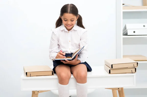 공부를 즐기는. 여자 아이 흰색 배경의 더미 근처 테이블에 앉아 있는 동안 책을 읽습니다. 여 학생 공부 하 고 책을 읽고 즐길 수 있습니다. 아이 학교 유니폼 웃는 얼굴이 좋아하는 문학 읽기 — 스톡 사진