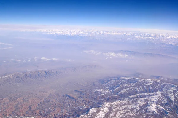 Het oppervlak van de aarde met besneeuwde bergen op blauwe hemel, luchtfoto. Bescherming van het milieu en ecologie. Berglandschap. Ontdekking en avontuur. Dag van de aarde elke dag — Stockfoto
