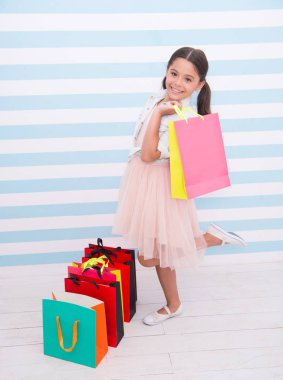 Şirin fashionista. Çocuk kız alışveriş torbaları çizgili bacground taşır. Her yaştan kadınlar alışveriş tapıyorum. Memnun yüz gülümseyen kız çanta yeni giysileri ile tutar. Çocuk kız zevk alışveriş satış sezonu