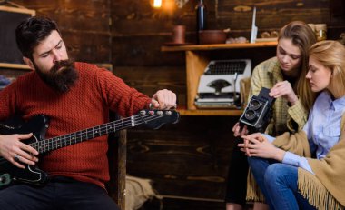 Müzisyen trendy hipster sakal ve bıyık gitar çalmak. Sakallı adam ayarlama müzik aleti. Anne ve kızı Baba müzik, hobi kavramı beste yaparken eski video kamera ile ilgili