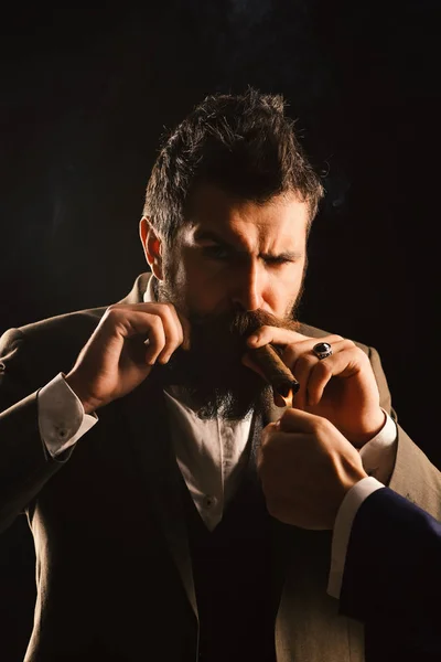 Человек с бородой держит сигару на черном фоне. — стоковое фото