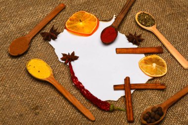 Mutfak tarifi kavramı. Çul arka plan üzerinde kağıt parçası. Tarçın, kurutulmuş portakal ve biber, anasonu boş kağıt, tarifi, kopya alanı çevresinde. Baharat kaşıkla beyaz kağıt yatıyordu