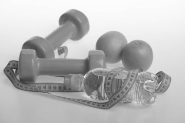 Yeşil renkli dambıllar, su şişesi, mezura ve meyve.