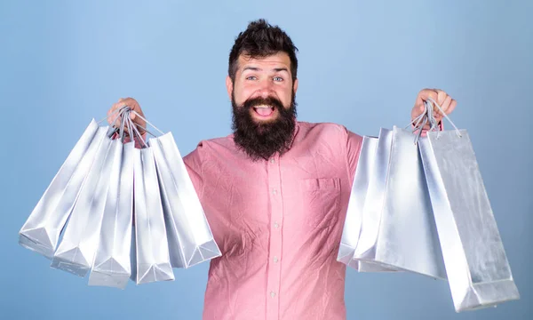 Typen, die in der Verkaufssaison mit Rabatten einkaufen. Verkauf und Rabattkonzept. Hipster mit glücklichem Gesicht sind shoppingsüchtig oder shopaholic. Mann mit Bart und Schnurrbart hält Einkaufstaschen, hellblauer Hintergrund — Stockfoto