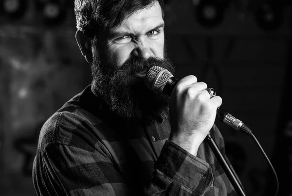 Musiker mit Bart und Schnurrbart, der im Karaoke Lieder singt. Rockstar-Konzept. Der Typ singt gern aggressiv. Mann mit enthusiastischem Gesicht hält Mikrofon, singt Lied, Karaoke-Club Hintergrund — Stockfoto