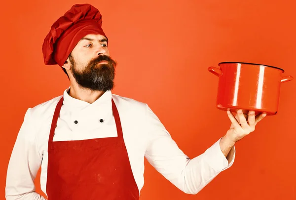 Man med skägg håller köksutrustning på röd bakgrund. — Stockfoto