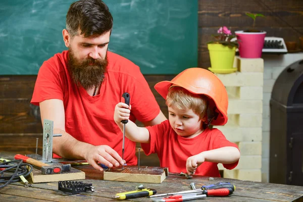 髭のツール ドライバーを使用しての小さな息子を教える親の父。少年は、保護用のヘルメットをパパと一緒にドライバーを使用する学習で忙しい子。チームワークと支援のコンセプト — ストック写真