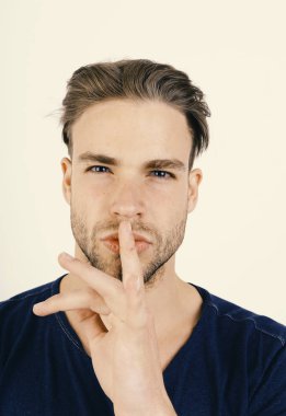 Koyu mavi tişörtlü adam sessizlik işareti gösteriyor.