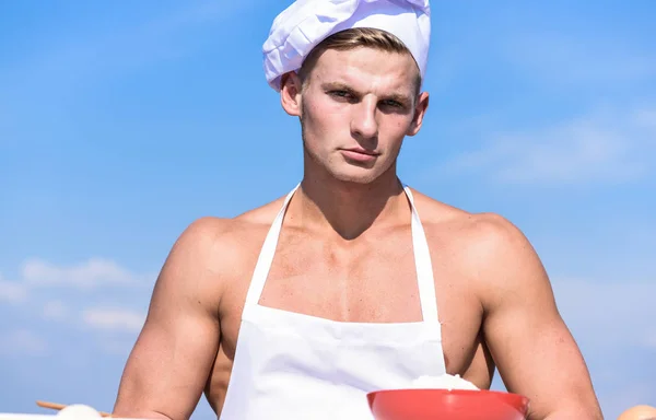 Man op vertrouwen gezicht draagt koken hoed en schort, sky op achtergrond. Mannelijkheid concept. Chef-kok met naakt sexy gespierd torso. Cook of chef-kok met gespierde schouders en borst ziet er aantrekkelijk — Stockfoto