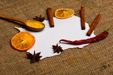 Tarçın, kurutulmuş portakal ve biber, anasonu boş kağıt, tarifi, kopya alanı çevresinde. Baharat kaşıkla beyaz kağıt yatıyordu. Çul arka plan üzerinde kağıt parçası. Mutfak tarifi kavramı