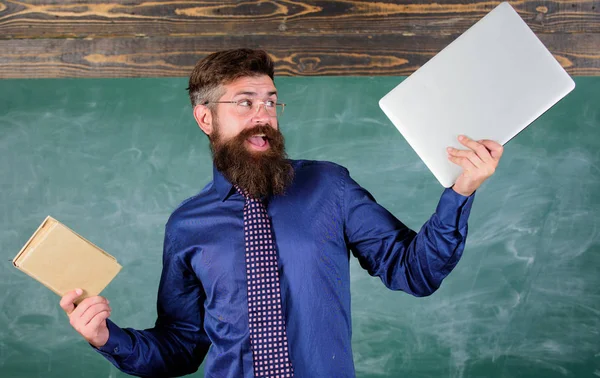 Que préfères-tu ? Professeur hipster barbu tient livre et ordinateur portable. Enseignant choisissant une approche pédagogique moderne. Livre de papier contre ordinateur portable. Numérique contre papier. Choisir la bonne méthode d'enseignement — Photo