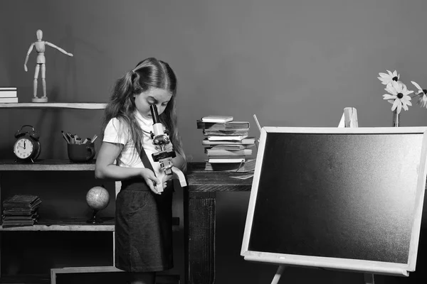 Estudante com cara ocupada na sala de aula. Menina olha para o microscópio — Fotografia de Stock