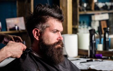 Berber makası ve tarak, elinde kapatın. Hippi saç modeli almak istemci sakallı. Berber kavramı. Salonların sandalye, salon arka plan sakallı adam. Kuaför saç kesme makinesi ile çalışır