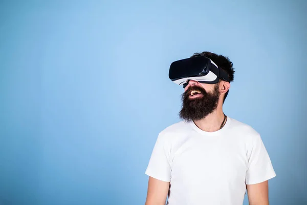 Hipster sul viso sorridente godere della realtà virtuale con gadget. Uomo con barba in VR, sfondo azzurro. Concetto tecnologico digitale. Guy con display montato sulla testa interagire nella realtà virtuale — Foto Stock