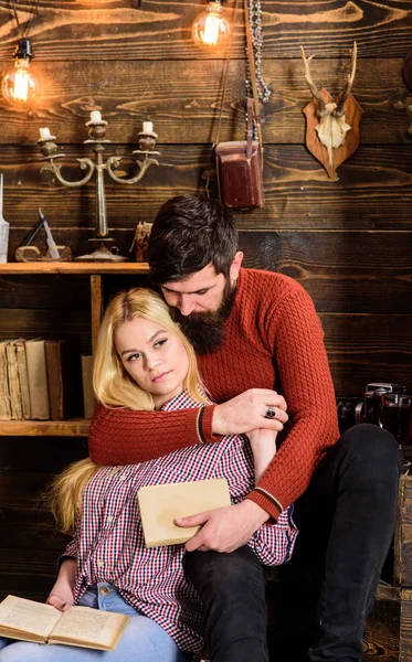 Romantic evening concept. Lady and man with beard on dreamy faces hugs and reading romantic poetry. Couple in love reading poetry in warm atmosphere. Couple in wooden vintage interior enjoy poetry