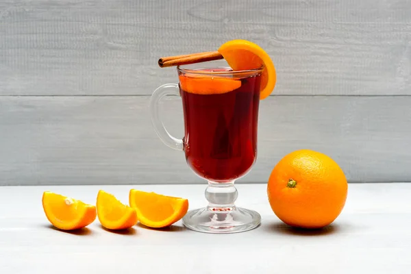 Drink or beverage with orange and cinnamon. Mulled wine with orange juice. Drink and cocktail concept. Glass with mulled wine near juicy orange fruit on white background, close up — Stock Photo, Image