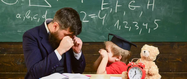 Kid cheerful boxing, beating dad. Playful child concept. Teacher and pupil in mortarboard, chalkboard on background. Father with beard, teacher teaches son, little boy, while child beating him — Stock Photo, Image