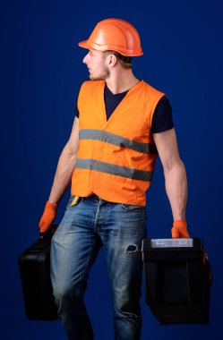 Kask, kask içinde adam araç kutusu ve araç, mavi arka plan ile bavul tutar. Donanımlı tamirci kavramı. İşçi, tamirci, tamirci, Oluşturucu profesyonel araçlar ile sakin yüz taşıdığı çanta üzerinde