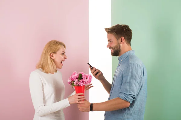 Online shop concept. Man use phone to buy anniversary gift online. Guy with phone and bouquet of flowers, pastel pink and green background. Man handsome nice giving flowers to his girlfriend — Stock Photo, Image
