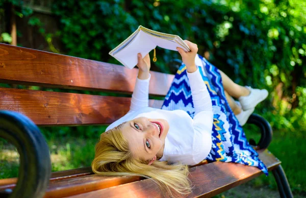 Interesante libro. Señora sonriente cara disfrutar del descanso. Chica leyendo al aire libre mientras se relaja en el banco. Chica yacía parque banco relajante con libro, fondo de la naturaleza verde. Mujer pasar el ocio con libro — Foto de Stock