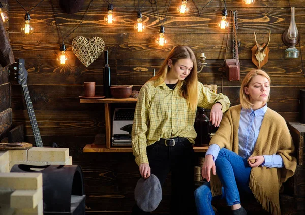 Amigos o hermanas pasan una agradable velada en la casa de guardabosques, fondo interior. Concepto de vacaciones en bosques. Las chicas en caras tranquilas disfrutan de un ambiente cálido mientras descansan. Las niñas disfrutan vacaciones — Foto de Stock