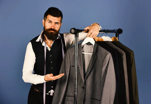 Modern wardrobe choice concept. Designer presents suit near clothes hangers. Man with beard