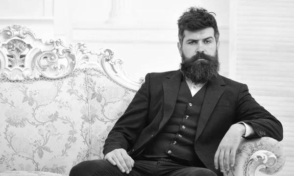 Hombre con barba y bigote con traje clásico, elegante atuendo de moda. Concepto masculinidad. Macho atractivo y elegante en serio, cara reflexiva sentado en el sofá de lujo a la antigua —  Fotos de Stock