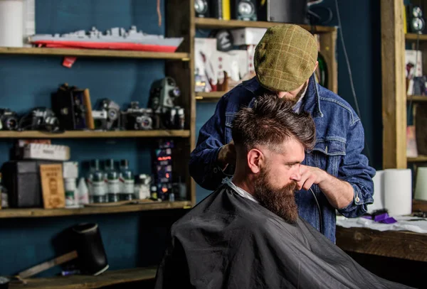 Um cliente Hipster a cortar o cabelo. Barbeiro com cortador de cabelo funciona no corte de cabelo do barbeiro barbudo fundo. Conceito de penteado Hipster. Barbeiro com clipper aparar o cabelo na nuca do cliente — Fotografia de Stock