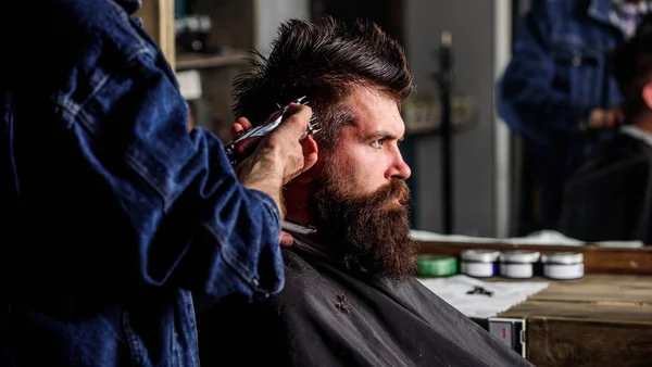 Il barbiere con tagliacapelli lavora sull'acconciatura per lo sfondo del barbiere. Concetto di stile di vita hipster. Barbiere che acconciano capelli di brutale cliente barbuto con clipper. cliente hipster ottenere taglio di capelli — Foto Stock