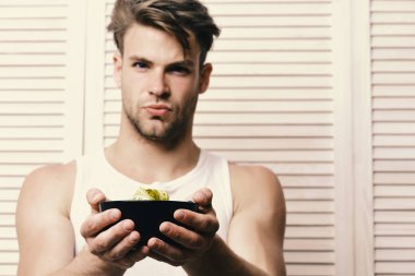 Beyaz kolsuz bluz giyen yemekleri sunmaktadır. Maço ciddi bir yüz ile sarı ölçü bandı ile kase tutar