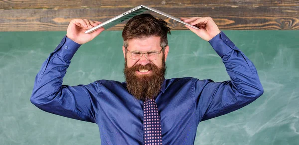 Teacher bearded man with modern laptop chalkboard background. Can not get used to teachers lifestyle. School blows his mind. Hipster teacher aggressive with laptop as roof goes mad about teaching