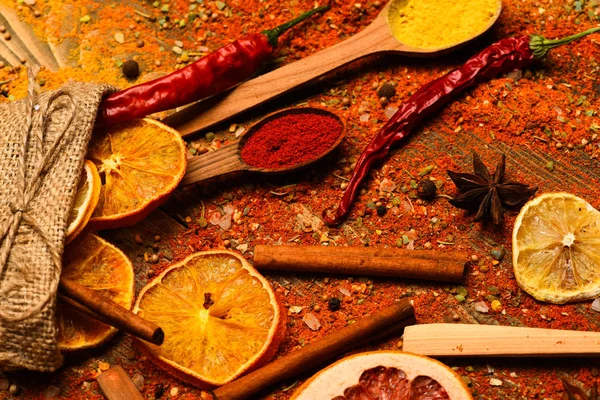 Spoons with spices on wooden texture. Spoons filled with cinnamon, grinded red pepper and curcuma powder and kitchen herbs scattered on table. Spices scattered all over wooden surface. Spices concept — Stock Photo, Image