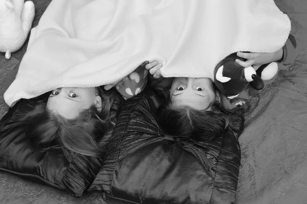 Girls have pajama party. Children with half hiddenfaces lie on bed, top view.