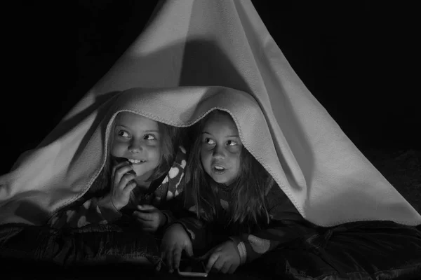 Les enfants font la fête en pyjama. Les filles aux visages effrayés se trouvent sous une tente de couverture rose — Photo