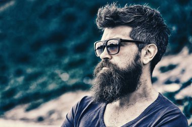 Berber ve stil kavramı. Sakal ve bıyık katı yüz, Doğa arka plan, defocused olan adam. Sakallı adam modern güneş gözlüğü takıyor. Sakallı hippi açık havada duran ise kendinden emin görünüyor