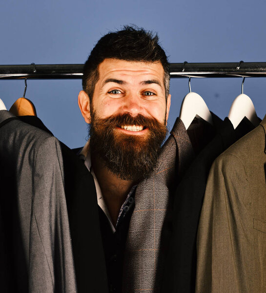 Продавец прячется среди костюмов на вешалках для одежды.